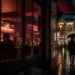 Rainy Vienna street at night with reflected lights and a warm lit bar window